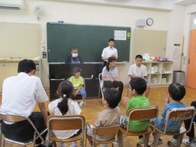 １枚の写真。教室に子どもたちが集まって輪になって椅子に座り、友達の話を聞いている様子。