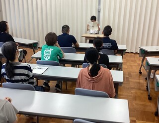 小学生が大勢の先生方の前で作文を読み上げている様子