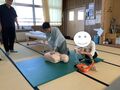 １名の女子生徒が胸骨圧迫を行い、その隣でAEDの準備をする女子生徒１名