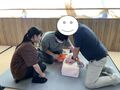 胸骨圧迫中を続ける中でAEDのパッドを貼る男子生徒