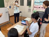 養護教諭が止血をするためにハンカチを指で押さえて心臓より高い位置にしているのを児童に提示している様子