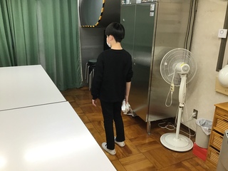 Oさんが食堂の床に掃除機をかけている様子。