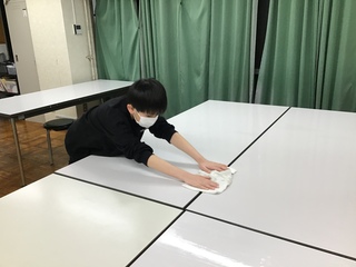 Oさんが食堂のテーブルに雑巾がけをしている様子。